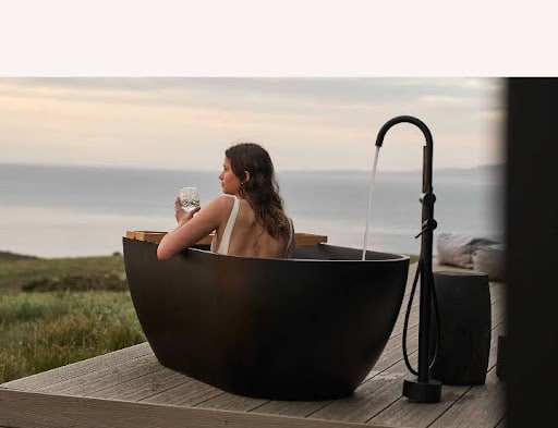 A CABN X guest relaxing in a freestanding outdoor bath while soaking up the views of the ocean at Kangaroo Island