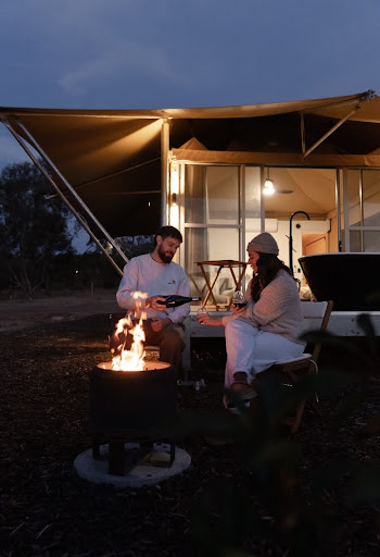 Couple enjoying a glass of red wine by a fire pit outside a cabin in the Barossa Valley at dusk